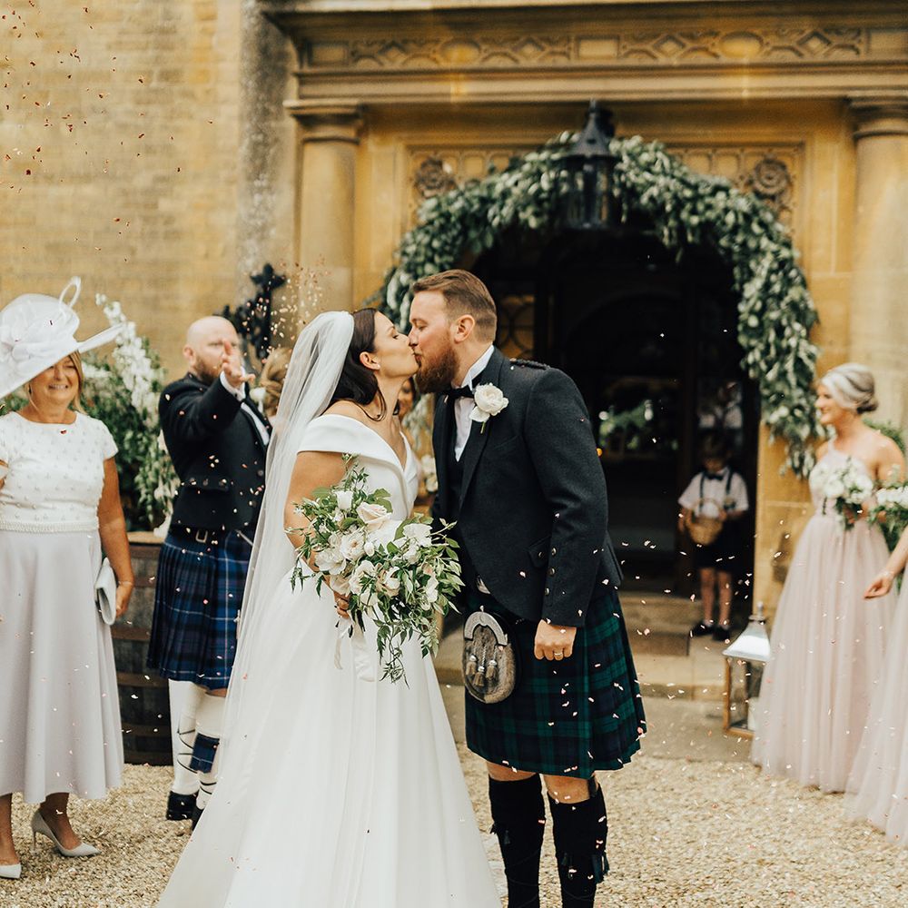 Confetti moment with Bride in a Suzanne Neville princess wedding dress kissing her groom in a tartan kilt at Foxhill Manor 
