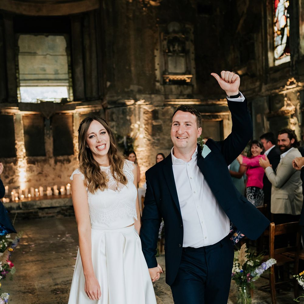 Bride in lacy wedding top and high low pleated skirt combo with groom in navy blue suit jacket and trousers 