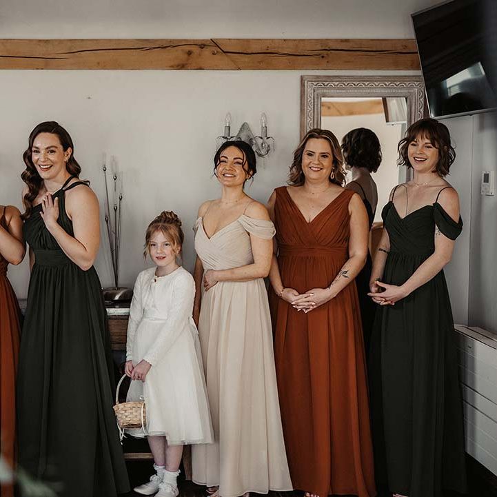 Bridesmaid in earth toned dresses with various neckline styles and flower girl in white dress with woven basket 