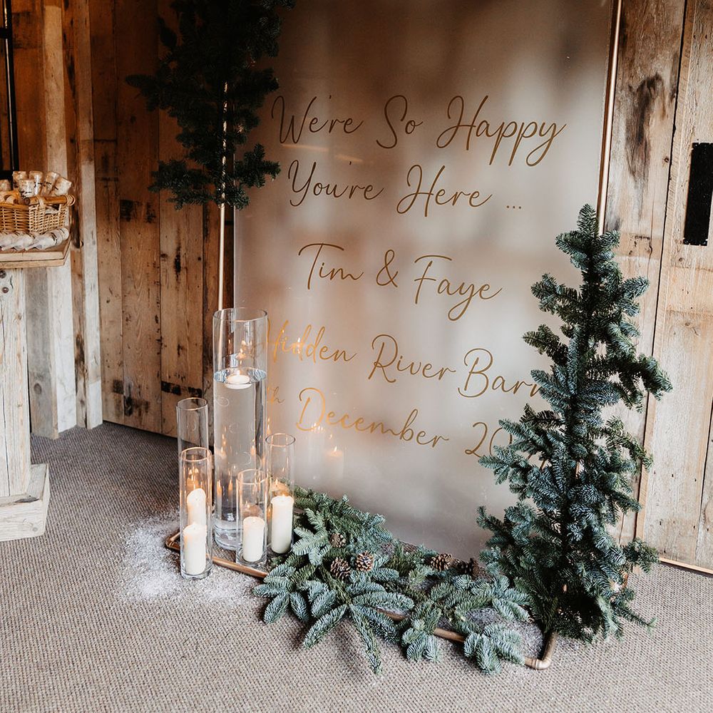 Large wedding welcome sign on frosted glass and gold font with candles and pinecone decorations 