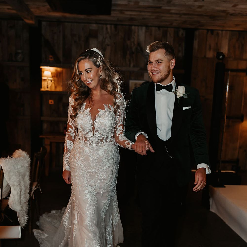 Bride in illusion lace fitted wedding dress walking hand in hand with groom in black tie green velvet suit jacket 