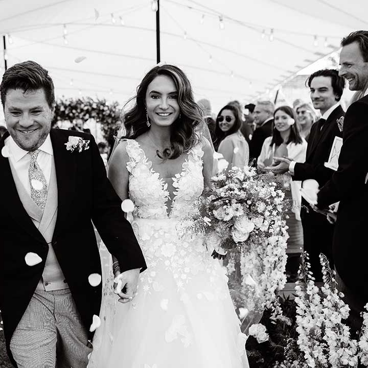 Bride and groom smile as they hold hands and walk back down the aisle as a married couple 
