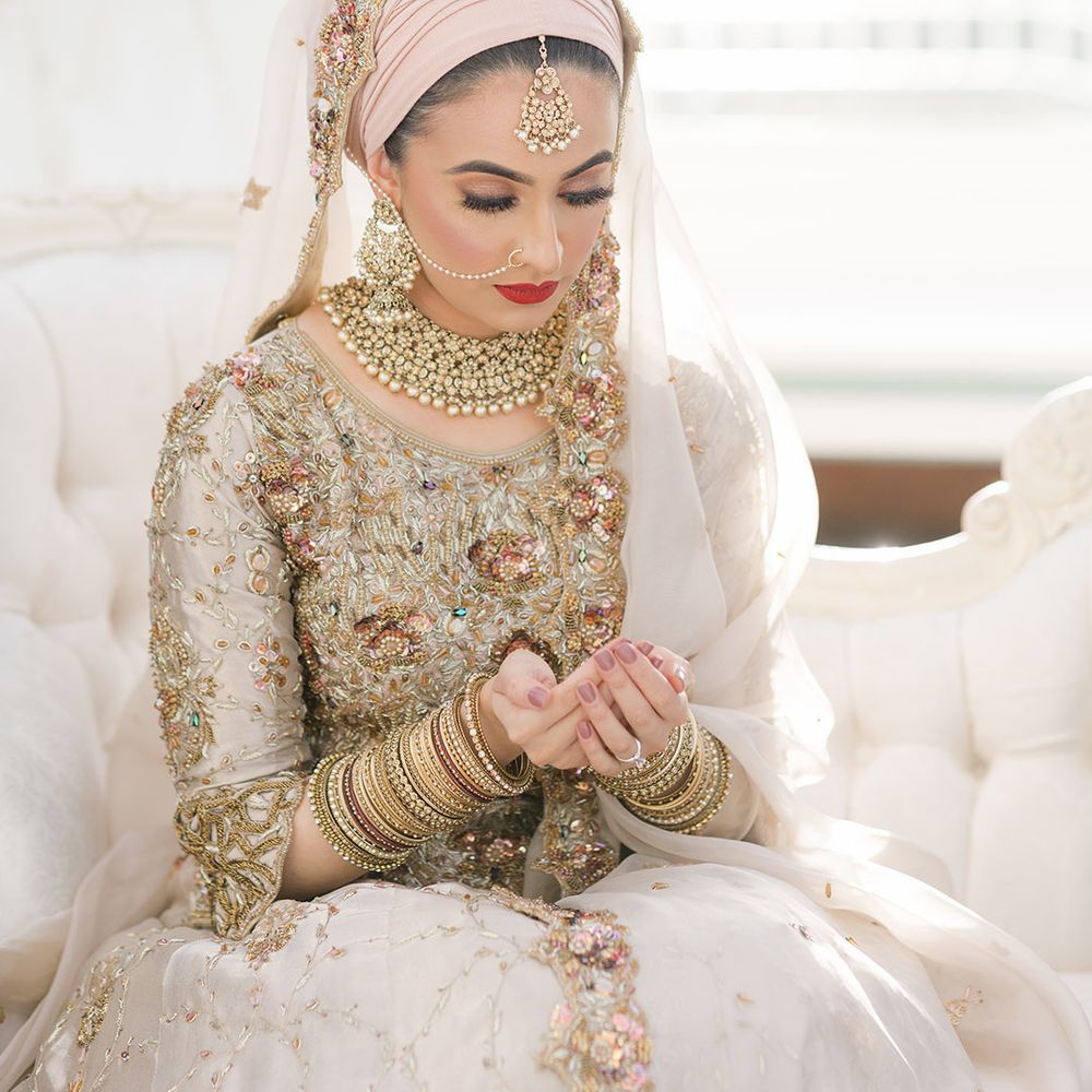 Bride cups her hands together whilst wearing traditional saree and gold bangles complete with purple nails and red lipstick 