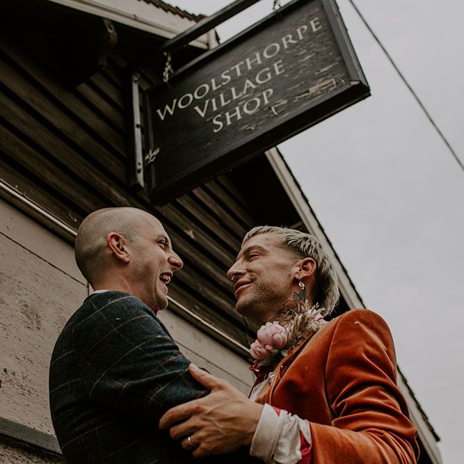 Grooms look lovingly at one another as groom wears velvet orange blazer 