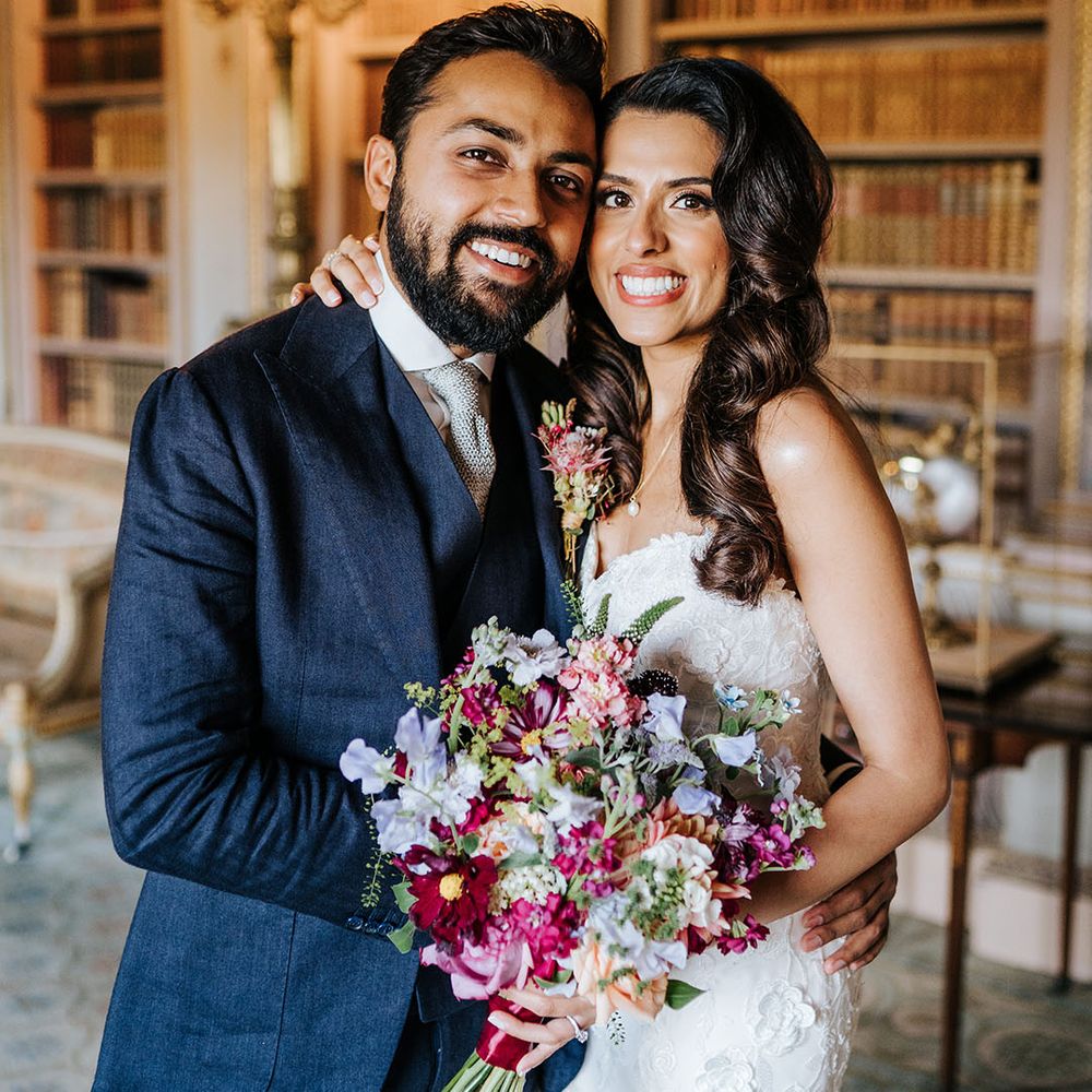 Bride holds brightly coloured floral bouquet and stands beside her groom who wears matching buttonhole 