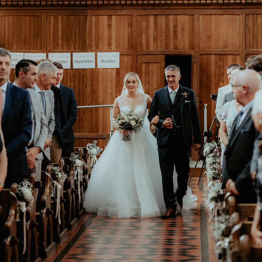 Father of the bride in a tweed suit walks the bride down the aisle for the church wedding