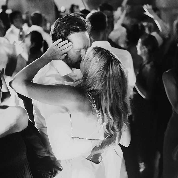 Bride and groom share a kiss ring their wedding party as guests dance 