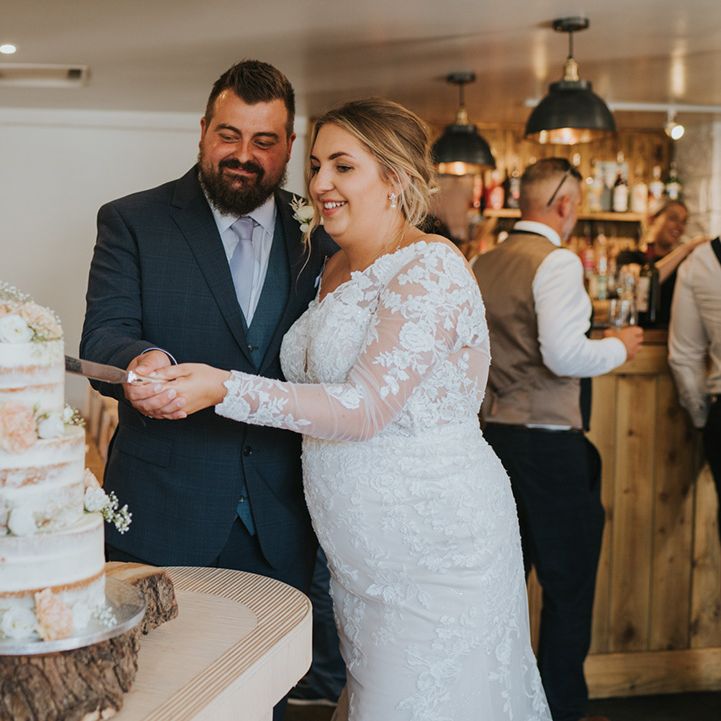 Bride & groom cut three tier naked wedding cake with floral decor 