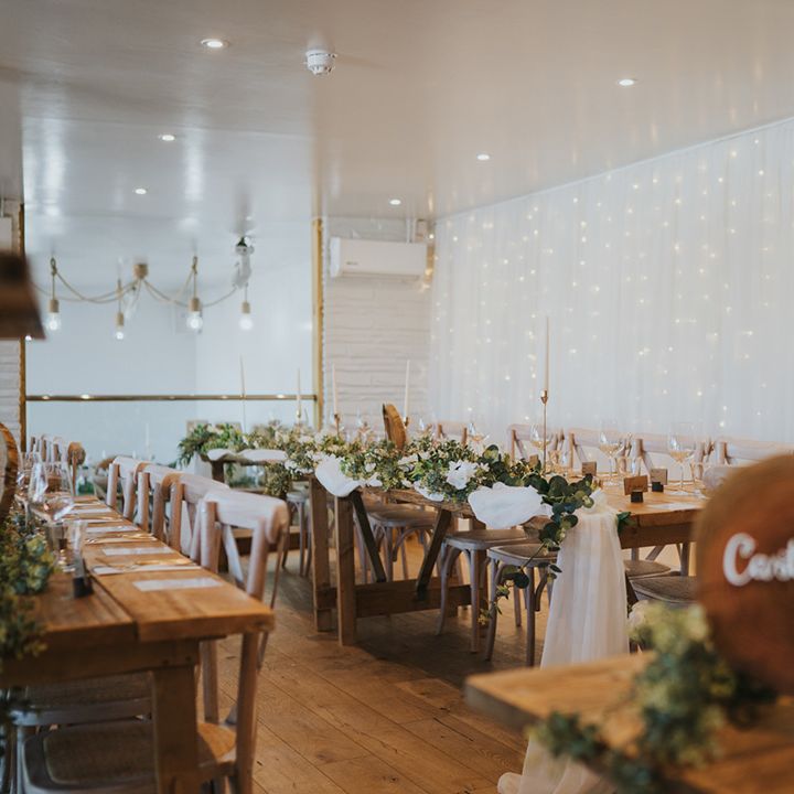 Fairy light canopy hangs from wall beside rustic banquet tables 