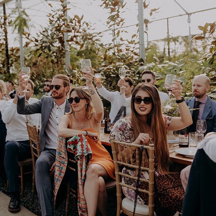 Seated guests in sunglasses raising their glasses to the Bride and Groom