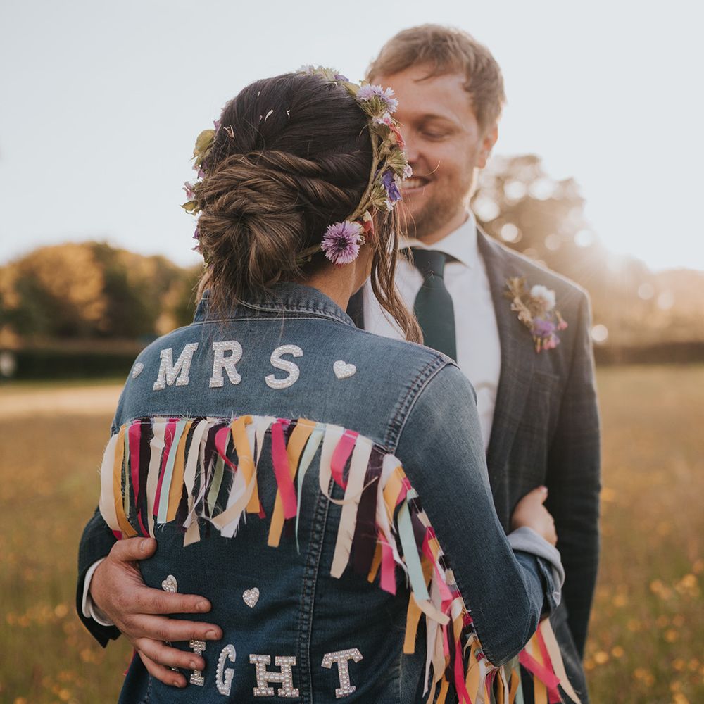 Bride wears her hair in low styled bun complete with colourful personalised denim jacket