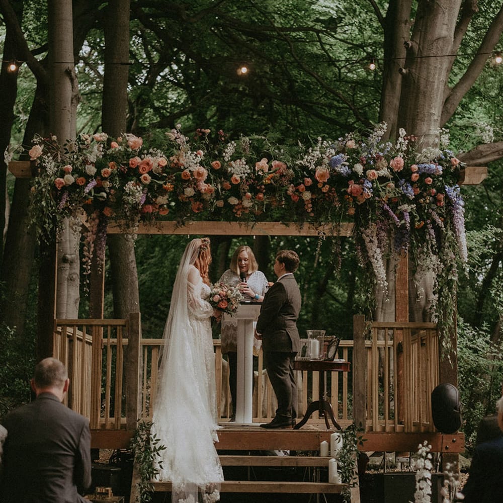 Blue, pink, and white wedding flowers decorating wooden gazebo at Lila's Wood wedding venue 