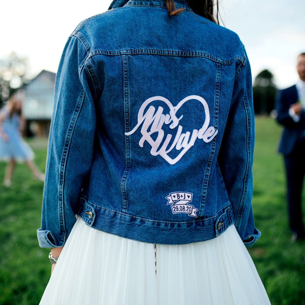 Bride in bright blue bridal denim jacket with love heart personalised motif with the initials and wedding date at the bottom 