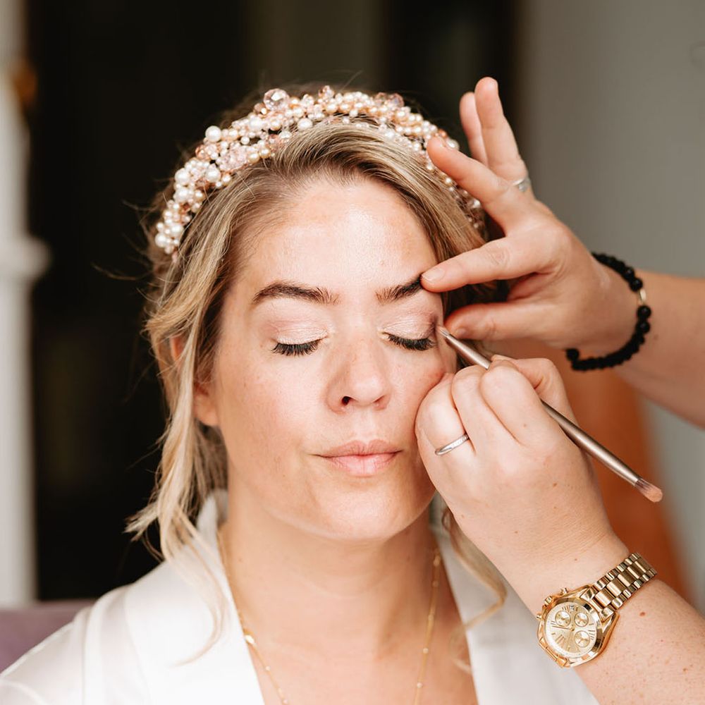 Bride wearing a pearl tiara gets her makeup done for the wedding day 