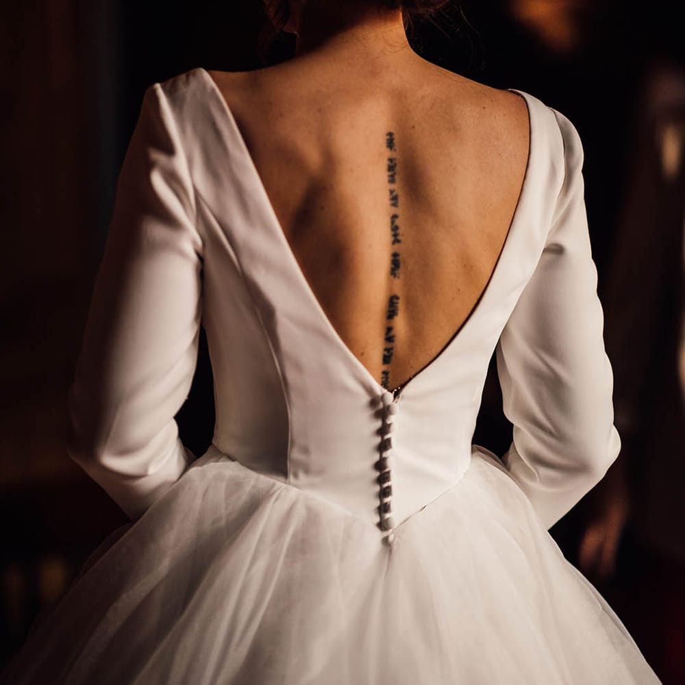 Bride wearing a long sleeve wedding dress with low back showing off her spine tattoo