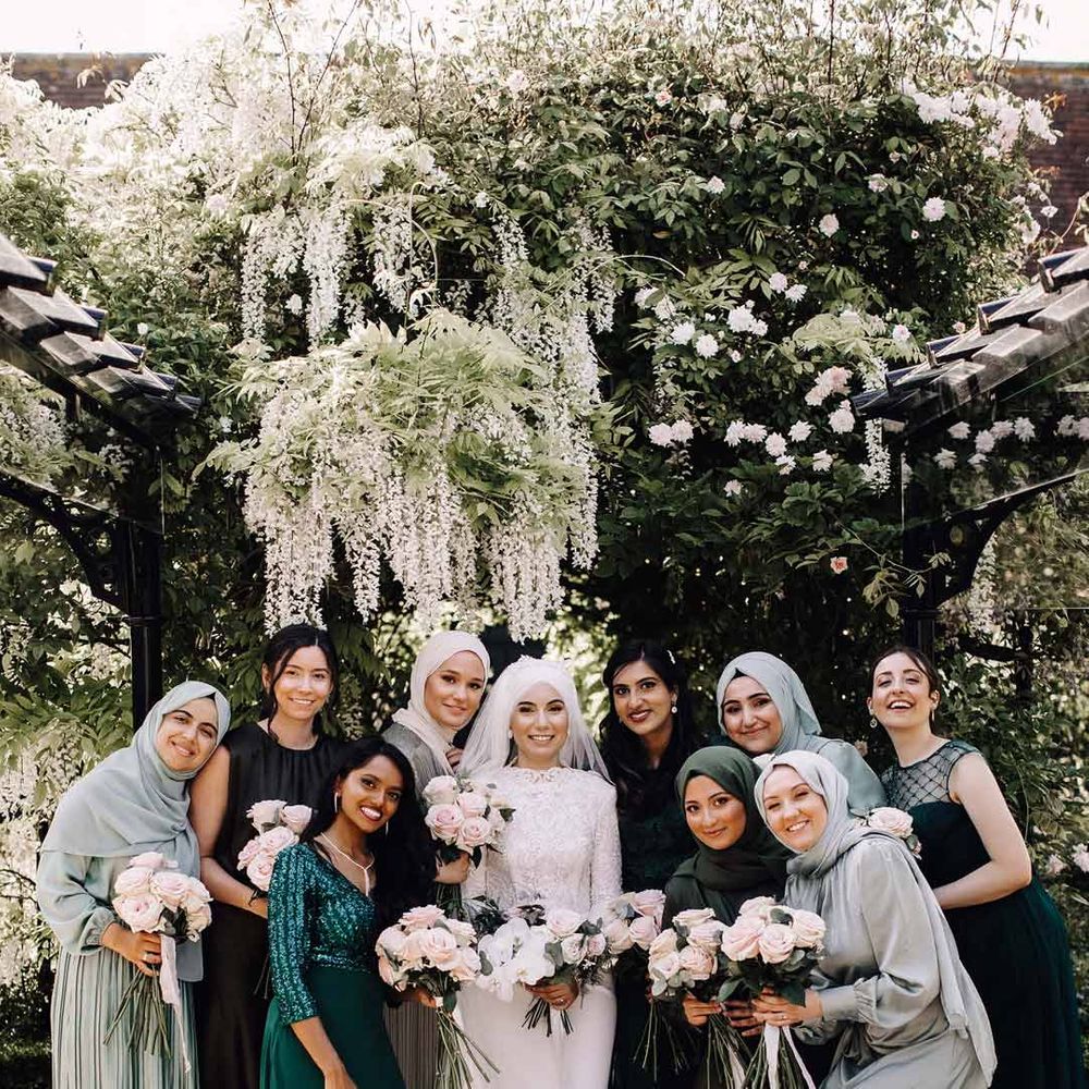 Bride in long sleeve lace wedding dress standing with bridesmaids in mismatched sage green, forest green and black bridesmaid outfits 