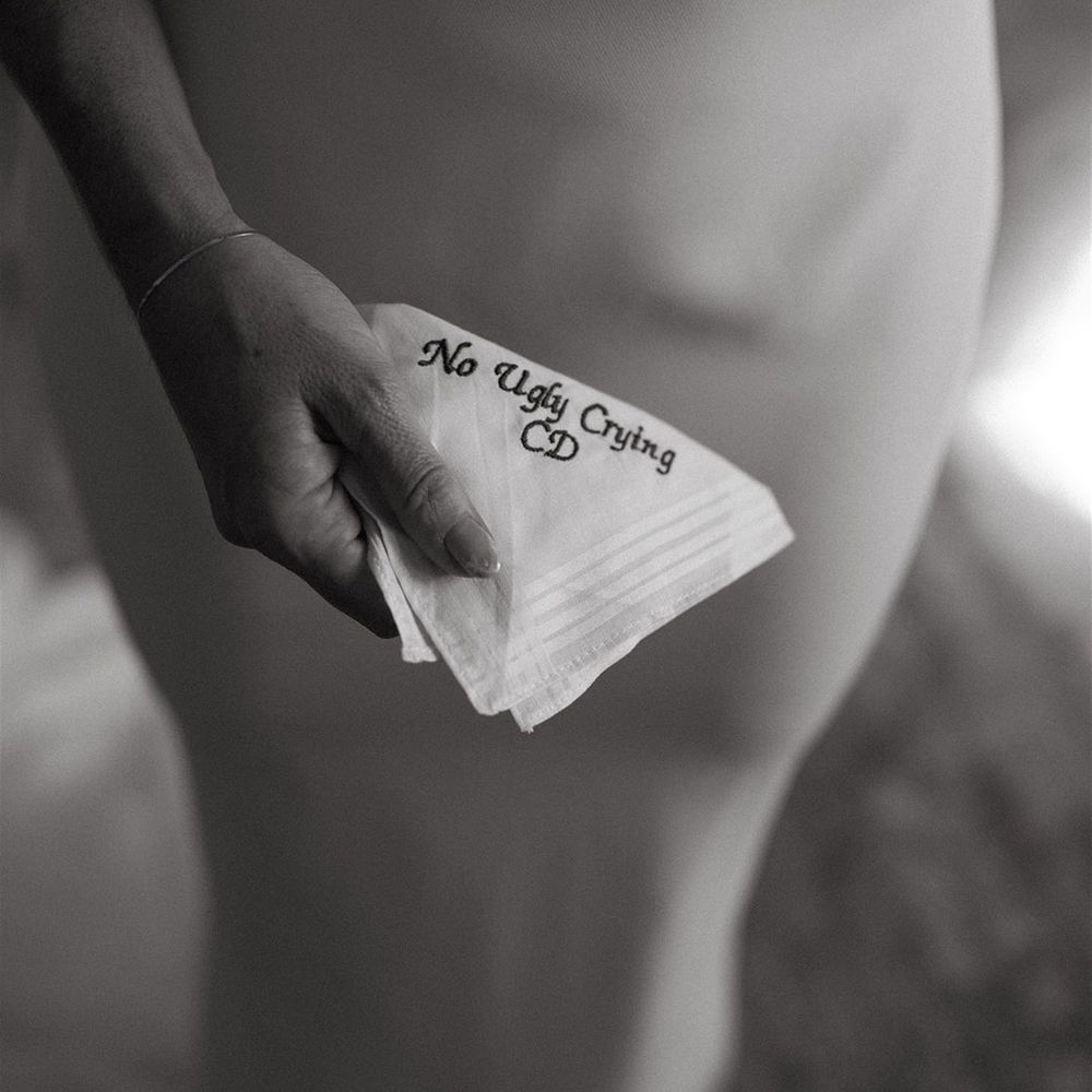 Bride holding embroidered wedding handkerchief reading 'no ugly crying' 