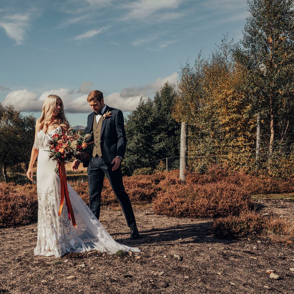 Bride walks in appliqué wedding gown carrying Autumnal bouquet tied with orange ribbon  