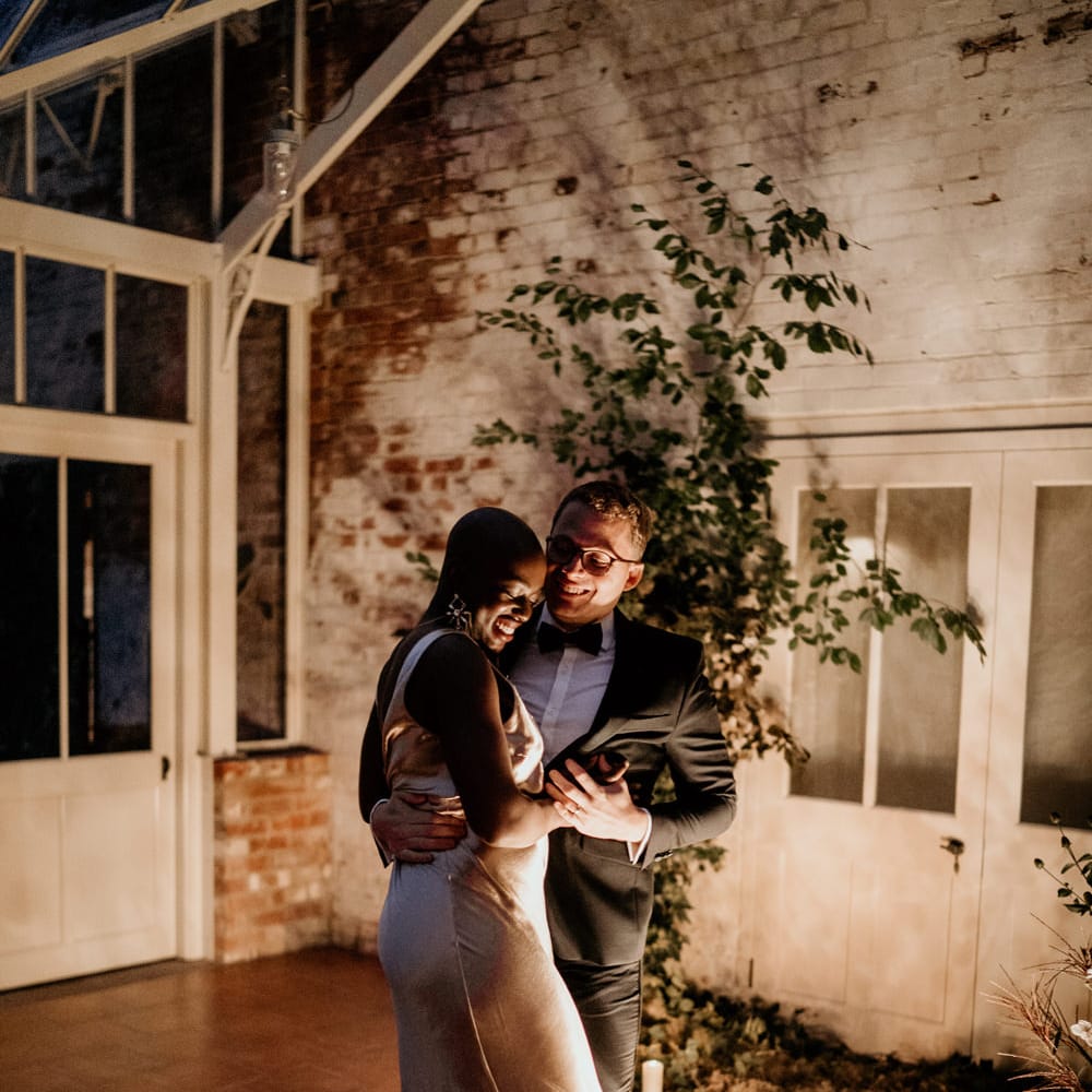 Bride with alopecia enjoying her intimate first dance on a wool rug surrounded by chandeliers 