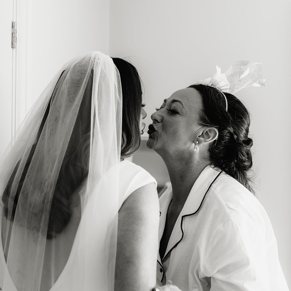Bride in white Made With Love wedding dress and veil embracing mother of the bride in satin shirt and shorts pyjama set