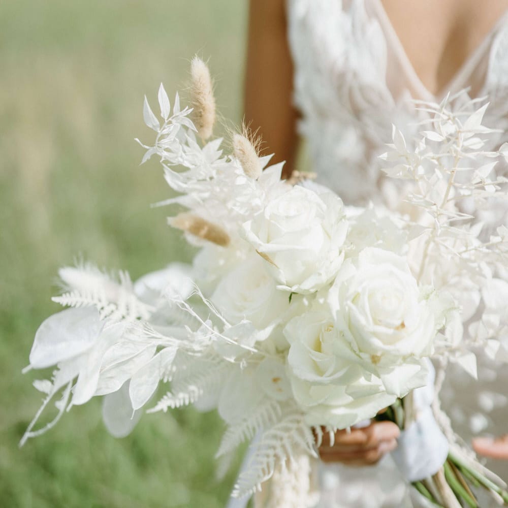 Bride holding all white bouquet including roses, pampas grass and white leaves