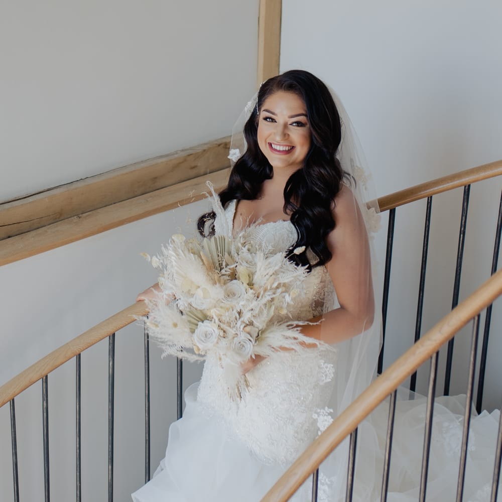 Beautiful bride in a strapless fishtail wedding dress walking down the stairs holding a dried flower wedding bouquet 