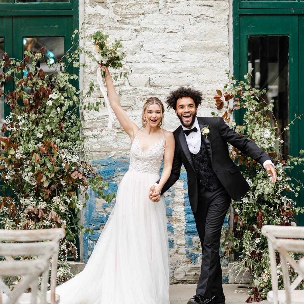 Bride in an embellished bodice and tulle skirt wedding dress holding hands with her groom in a three piece tuxedo at Torr Vale Mill in Derbyshire