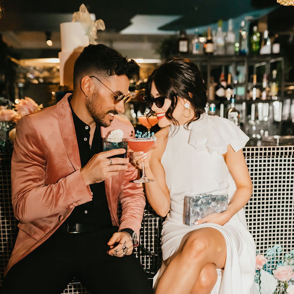 Stylish bride and groom sipping cocktails at the bar at their pink and teal city wedding 