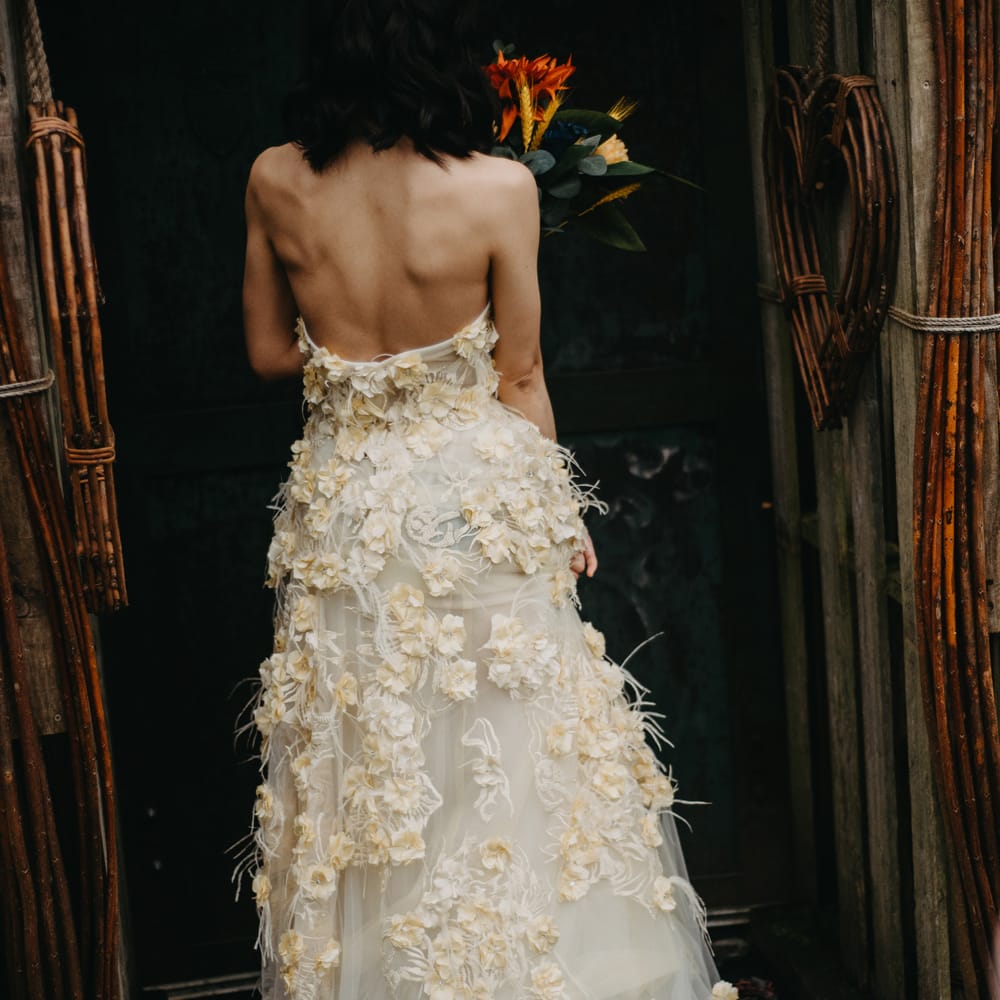Bride in strapless feathered appliqué wedding dress stands in doorway at rustic wedding in Lancashire