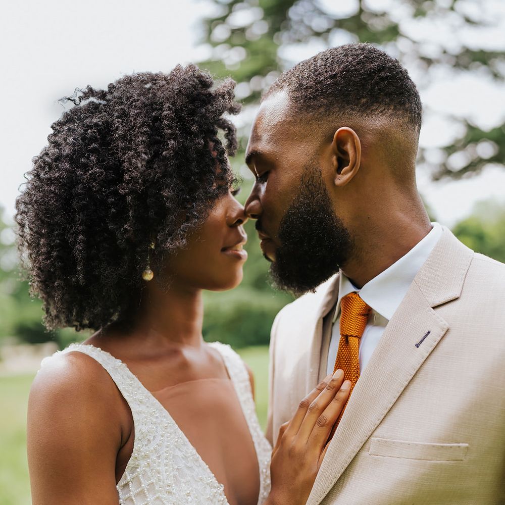 Black bride in an embellished plunging neckline wedding dress embracing her groom in a beige suit 