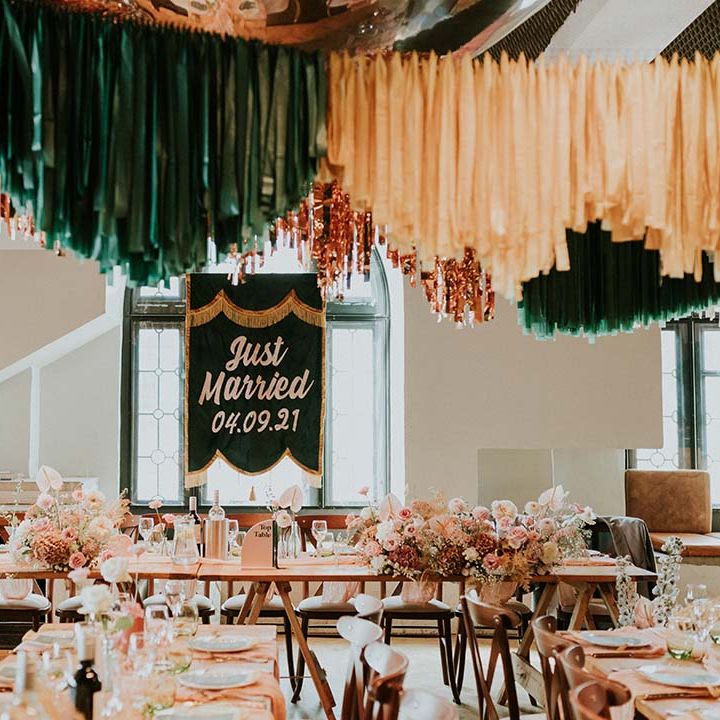 Green tassel Just Married banner sits at the top of reception venue complete with wooden tables 
