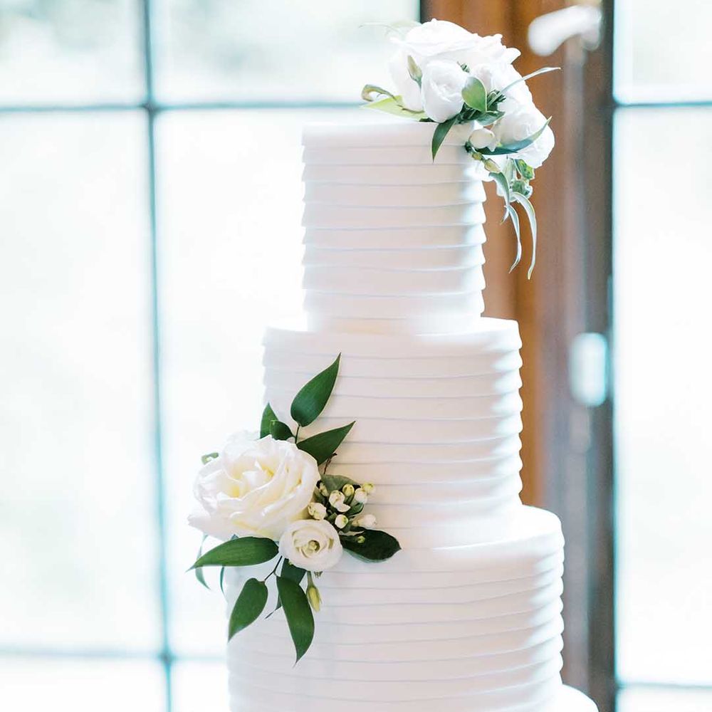 Elegant white wedding cake with white roses and foliage decor 