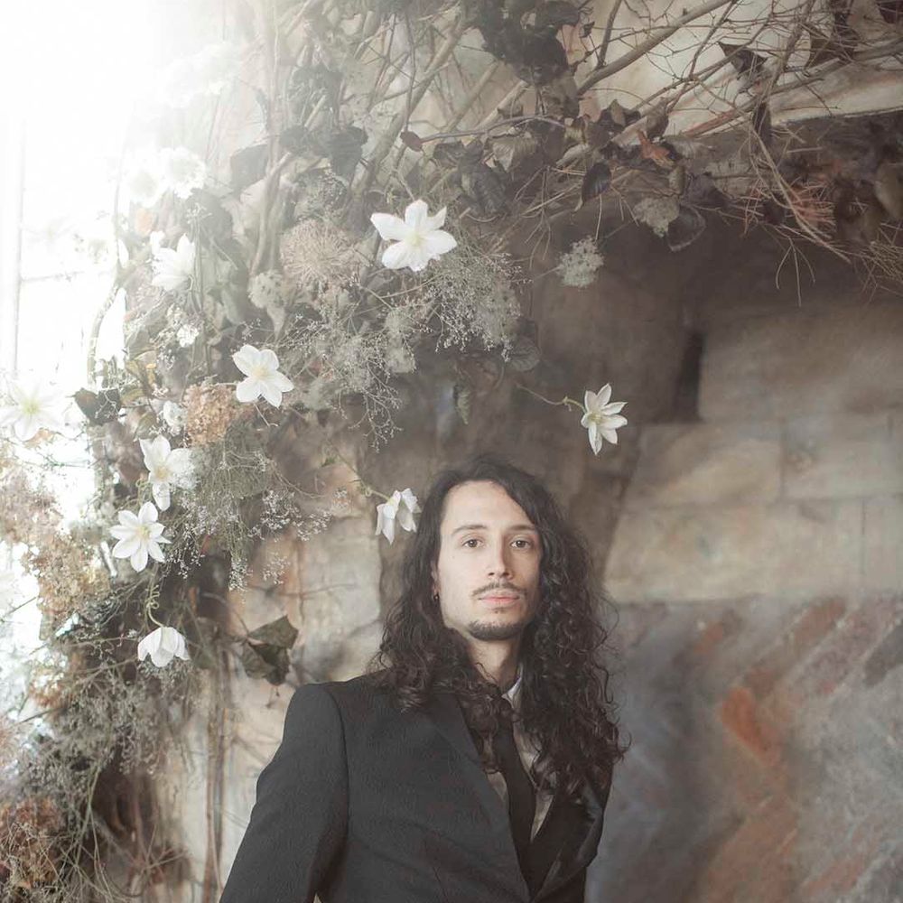 Stylish groom with long wavy hair and a beard wearing a dark wedding suit 