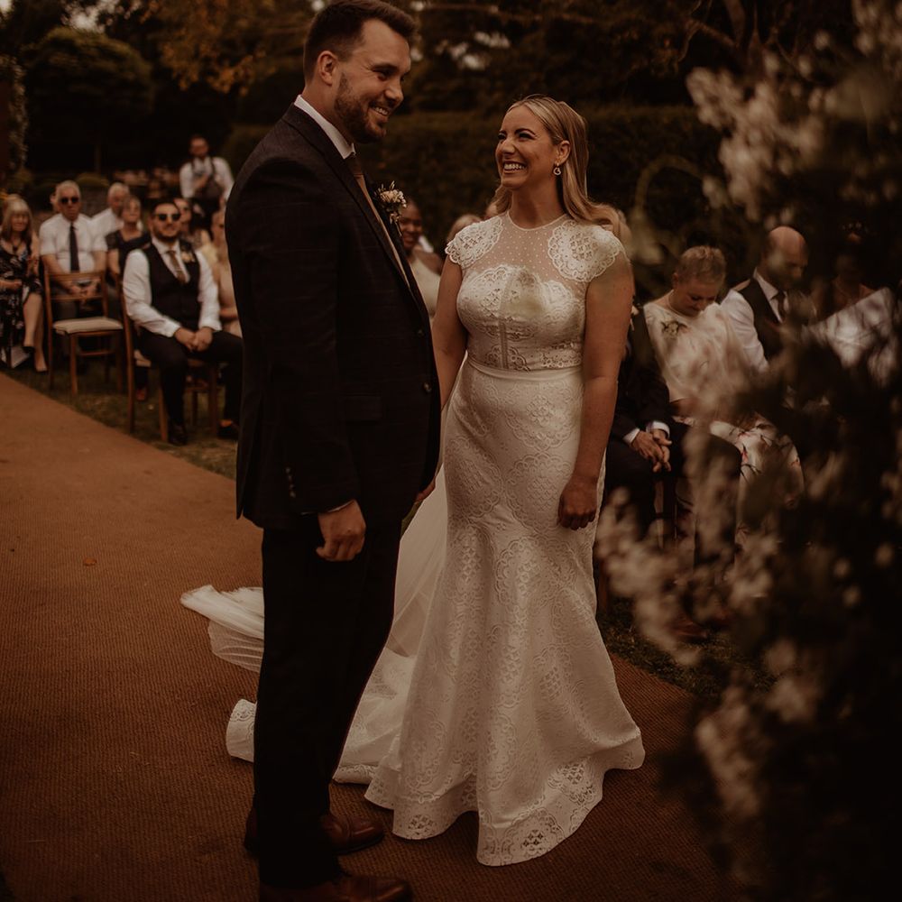 Bride in a Jesus Piero lace fishtail wedding dress with cap sleeves smiling at her groom during their outdoor Dewsall Court wedding 