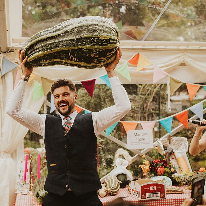 Groom in a navy waistcoat and floral tie holding up the winner of the best in marrow competition