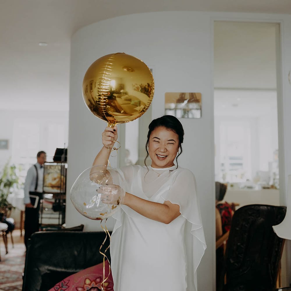 Bride holds gold balloon as she wears wedding dress sample complete with cape  | Irene Yap Photography