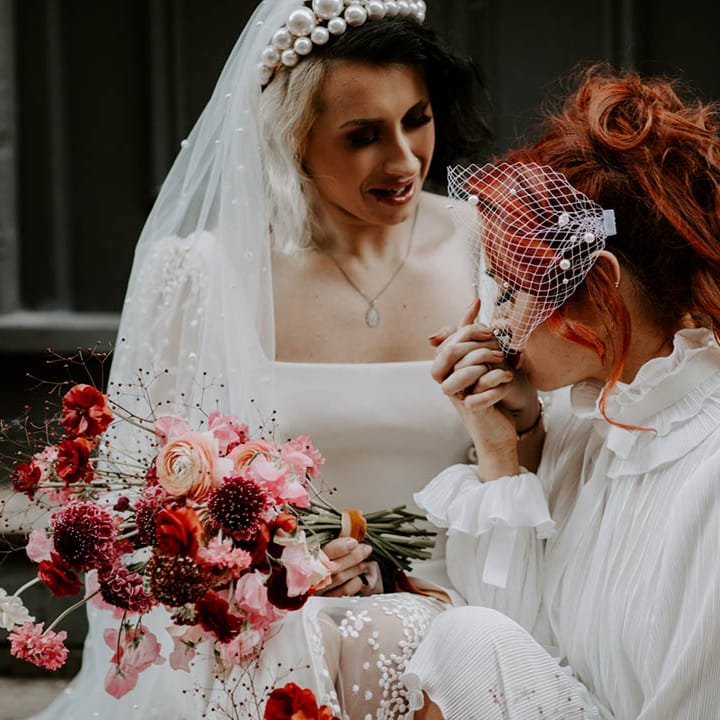 Bride in a high neck wedding dress with long sleeves and perl encrusted bidcage veil kissing her brides hand in a pearl headband 