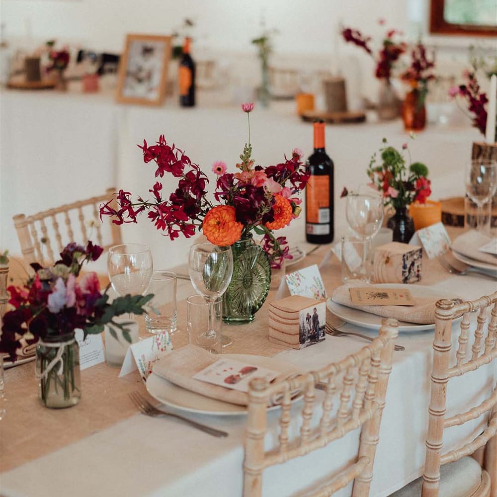 Colourful pink, red and orange wedding flower arrangements in green glass vases for wedding table settings 