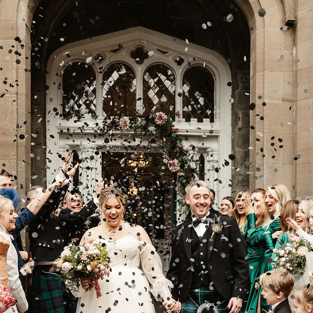Bride in sheer sleeved off the shoulder wedding dress with groom in black tie and kilt have confetti exit with black circle confetti