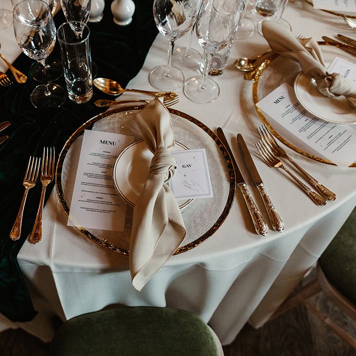 Table setting with white card with hand and stars on for name place card, green table runner and gold cutlery and plate with black candles