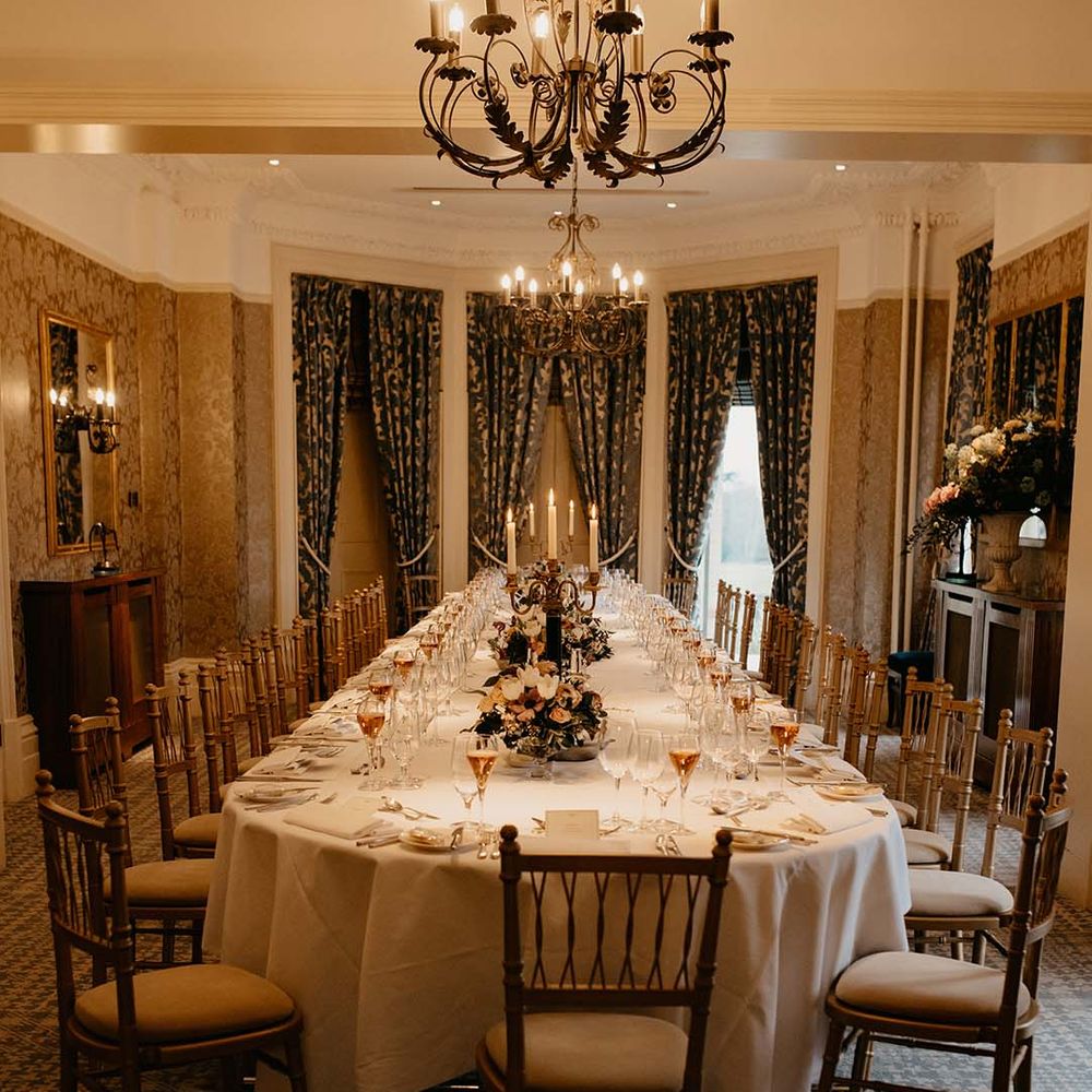 Large wedding tablescape with neutral mixed floral displays, wine glasses full and large draping green and gold curtains