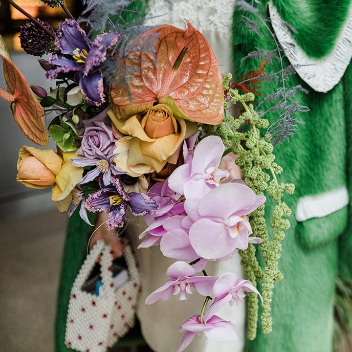 Pink, orange, yellow and purple wedding bouquet with roses and orchids next to bridal green fur jacket cover up