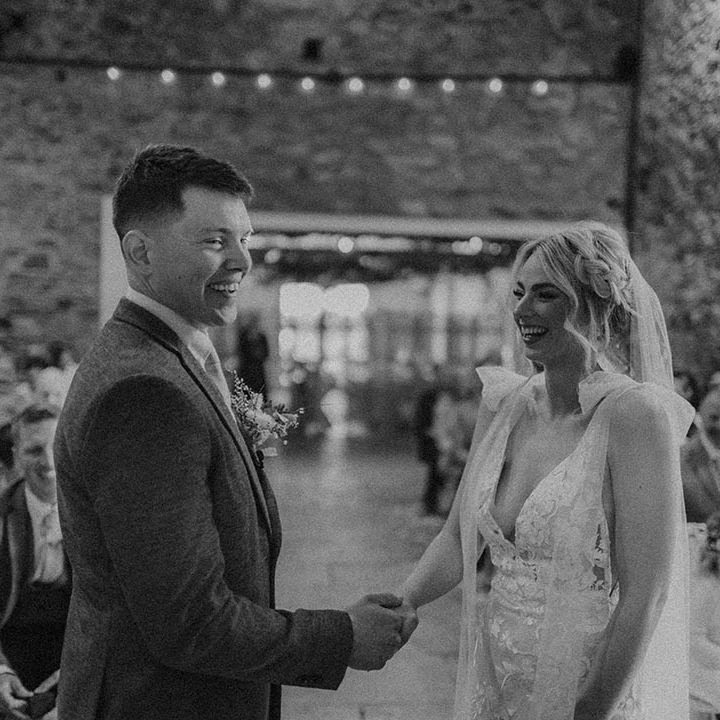 Bride in Made With Love wedding dress holding hands with groom as they both smile at the altar 