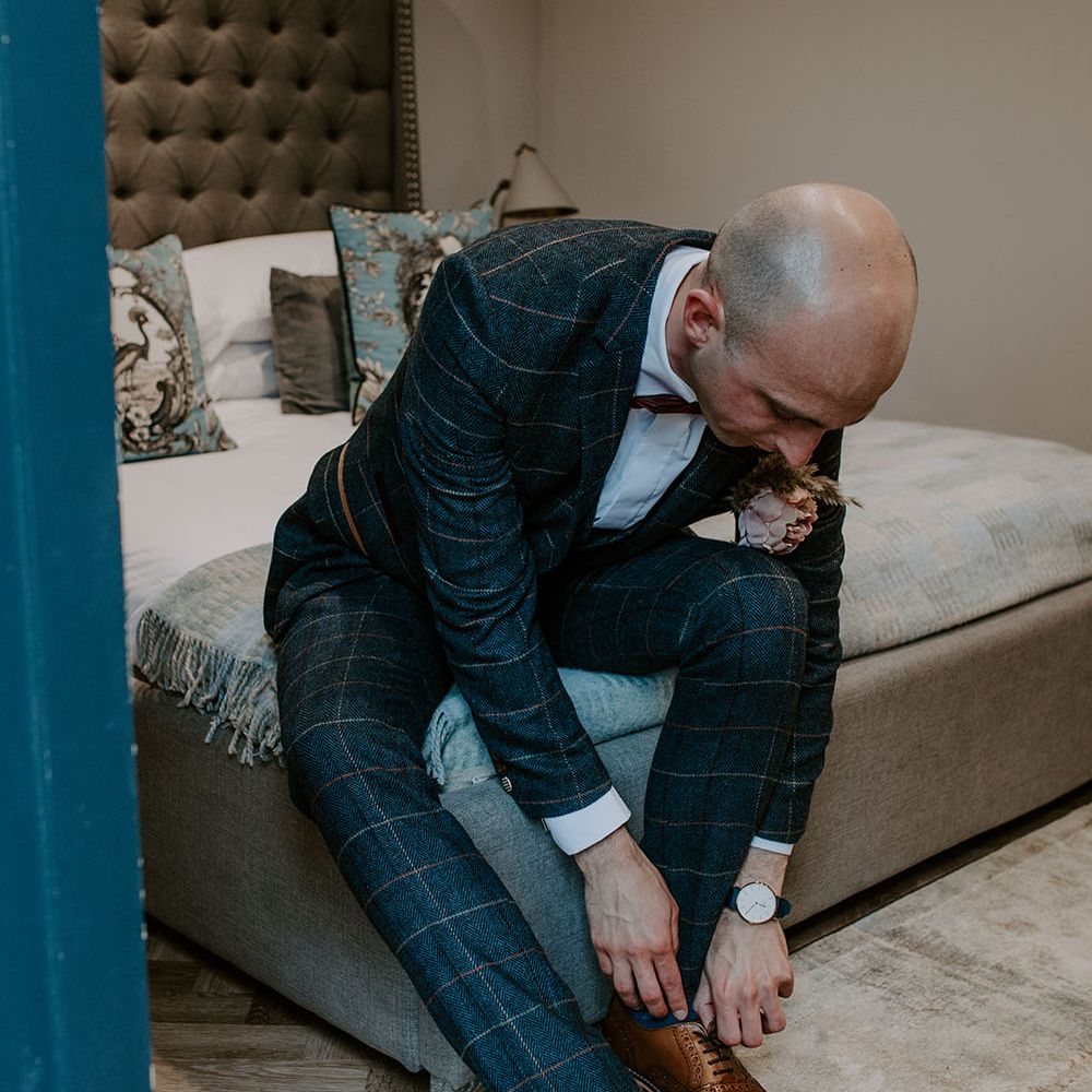 Groom wears homemade buttonhole whilst wearing tartan blazer and trousers complete with red bow tie 