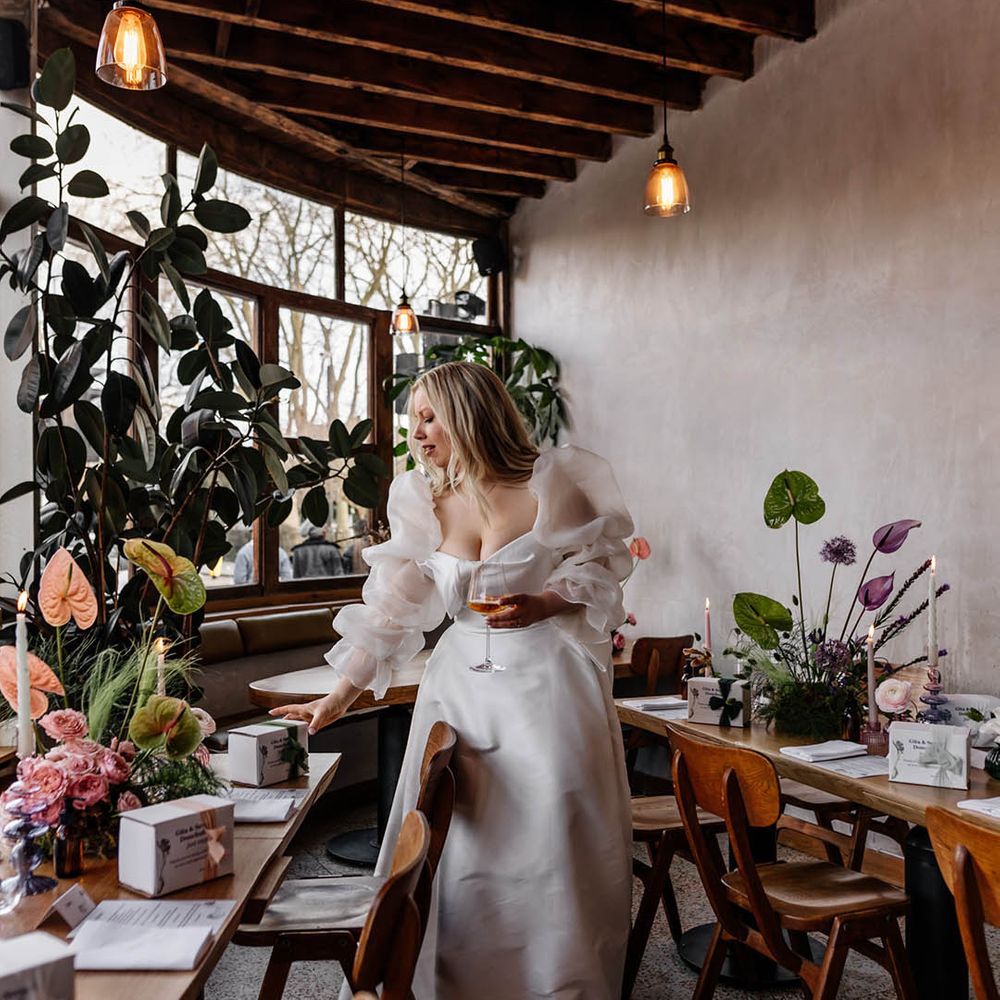 Bride in a JESUS PEIRO wedding dress with voluminous sleeves looking at the wedding reception table favours 