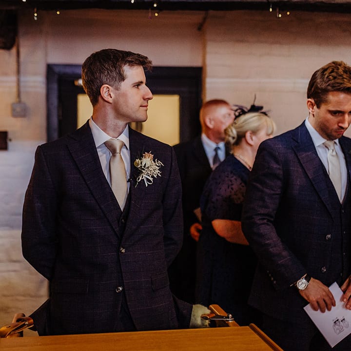 Groom wears a checkered su8it jacket and gold tie with a gold and white buttonhole for hotel wedding 