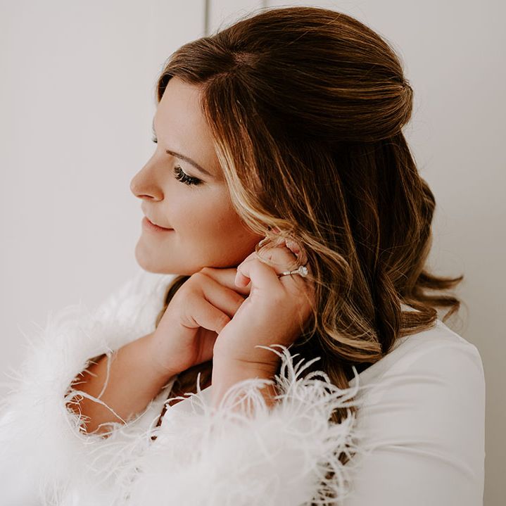 Bride wears silk pyjamas in white complete with fluffy cuffs as she puts in her earrings