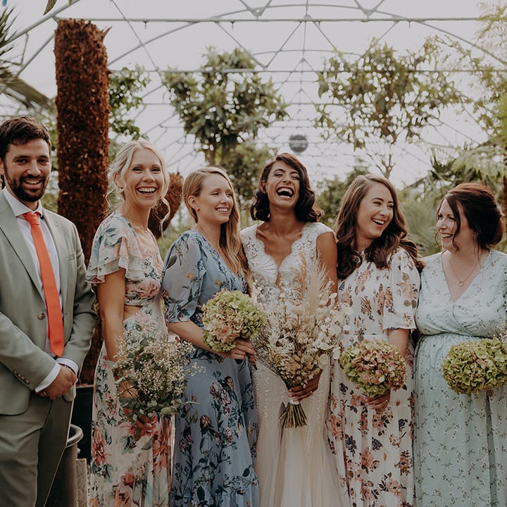 Bride poses with mixed gender bridal party wearing mixed floral dresses and a grey suit