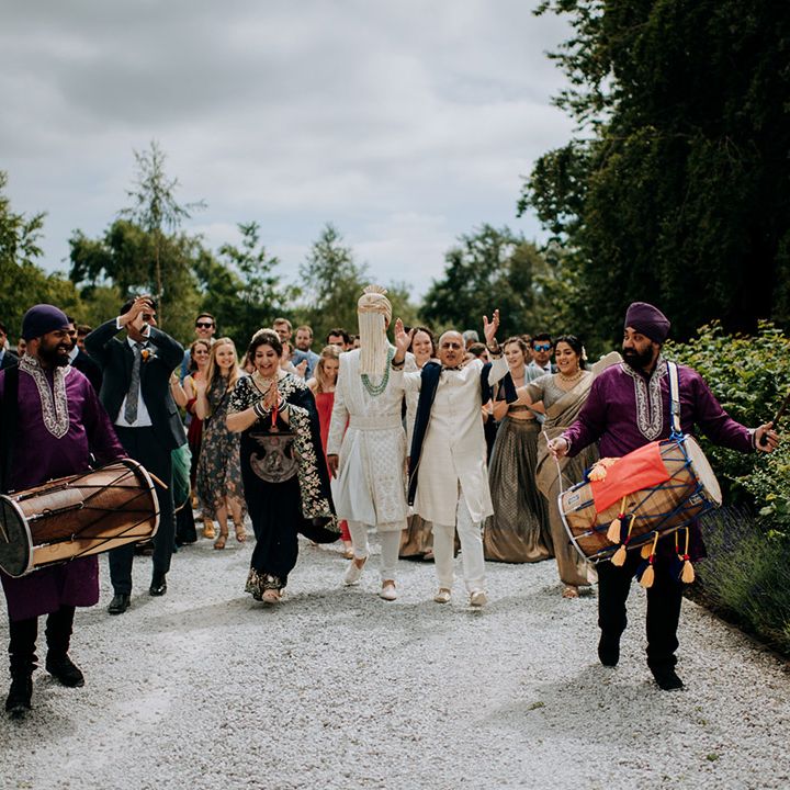 Groom walks with family as drummers play during wedding ceremony the Tithe Barn Bolton Abbey