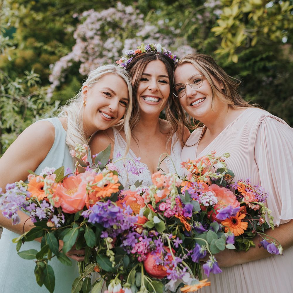 Bride stands with her bridesmaids holding colourful floral bouquets filled with peonies 